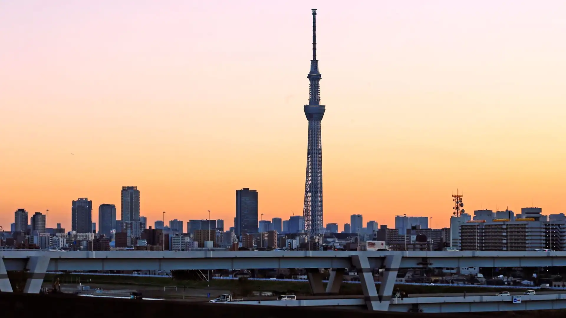Tokyo Skytree rising above the Sumida River at dusk, its lattice tower lit against the Tokyo skyline